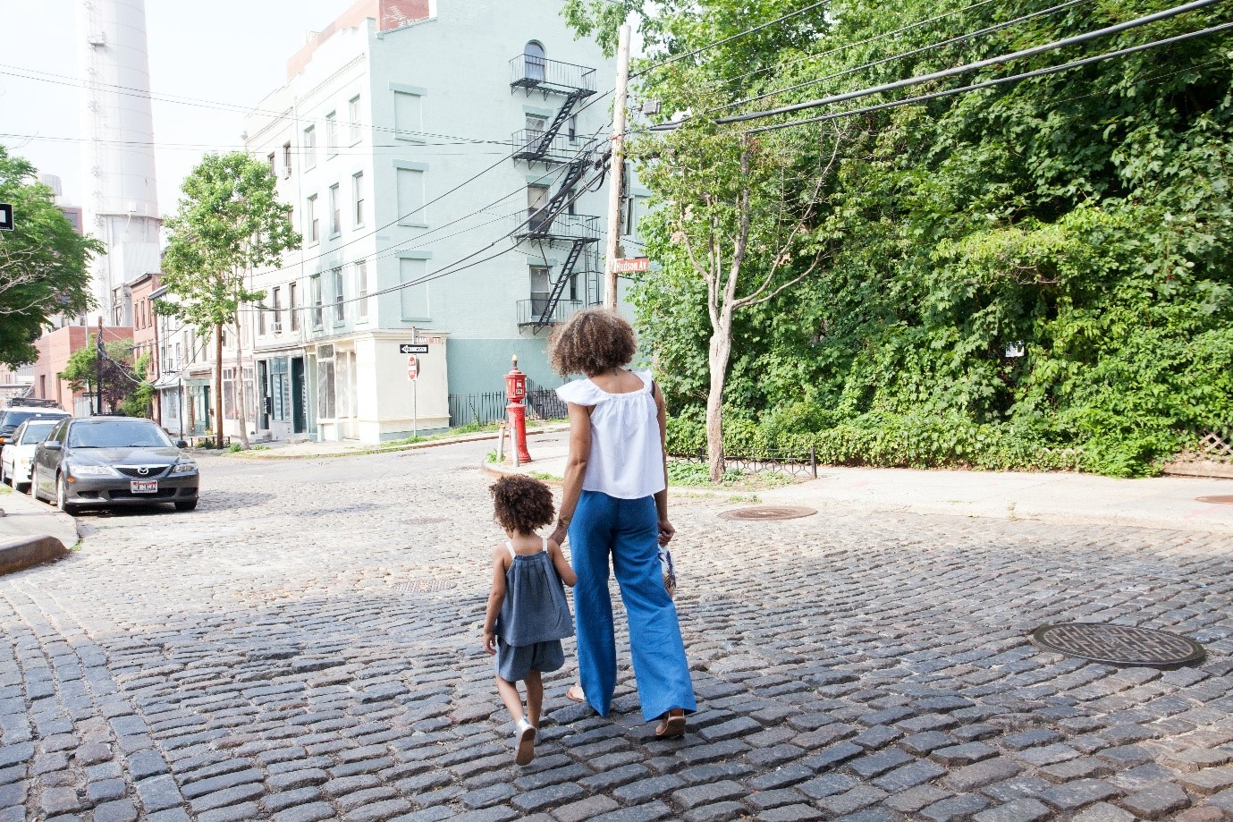 Photo of a woman walking with her back to the camera in a urban street while holding the hand of a young girl