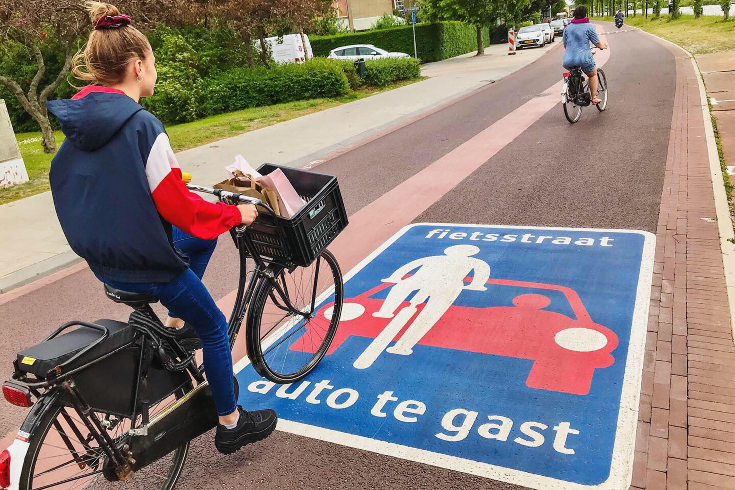 Photo of a young woman biking in a bike lane. On the pavement, there is the sign for cars to give priority to bikes