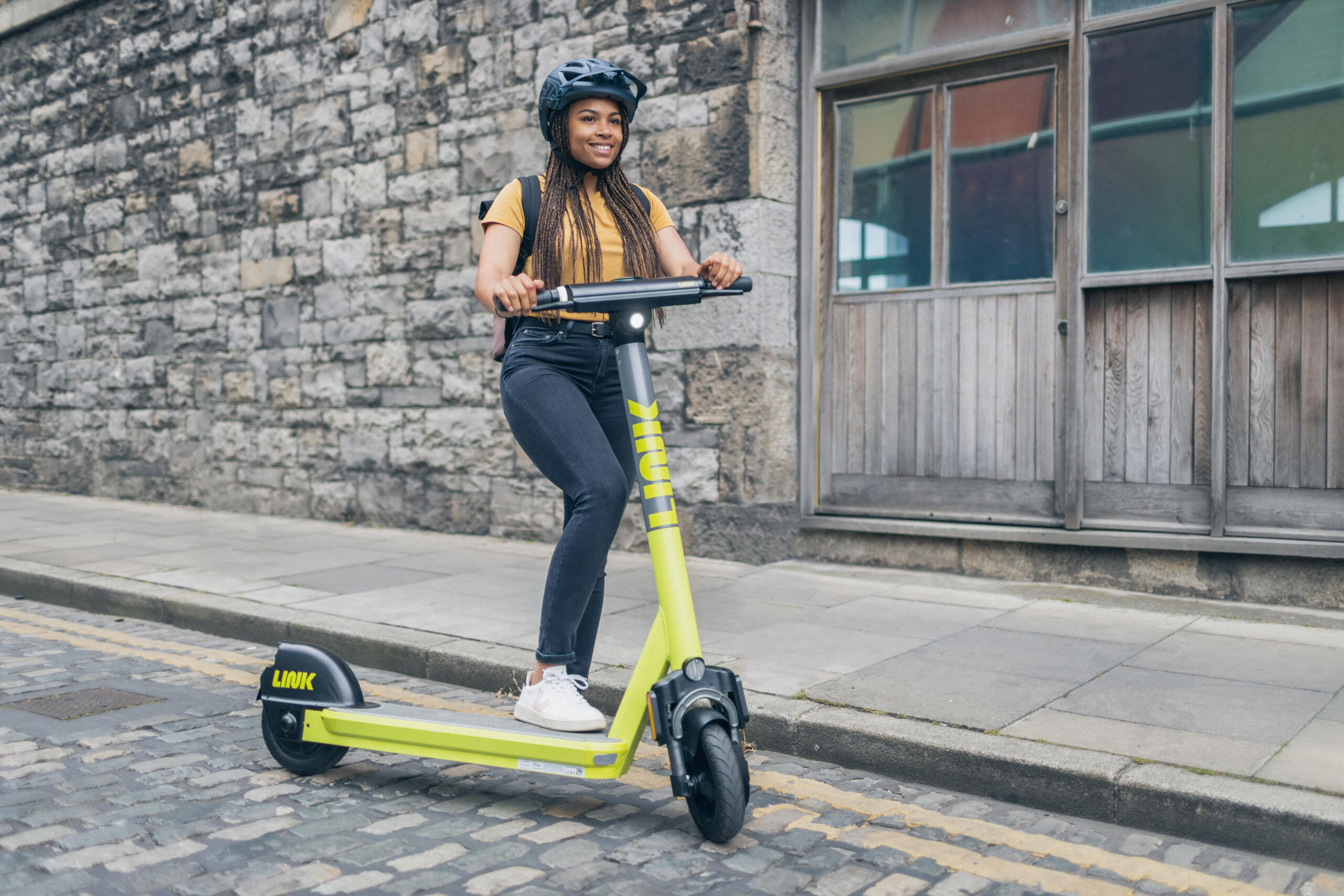 Photo of a young woman wearing an helmet and riding a scooter