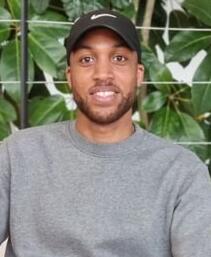Portrait photo of Nathan Ashley, he is a black young man with short hair, wearing a grey jumper and a black cap