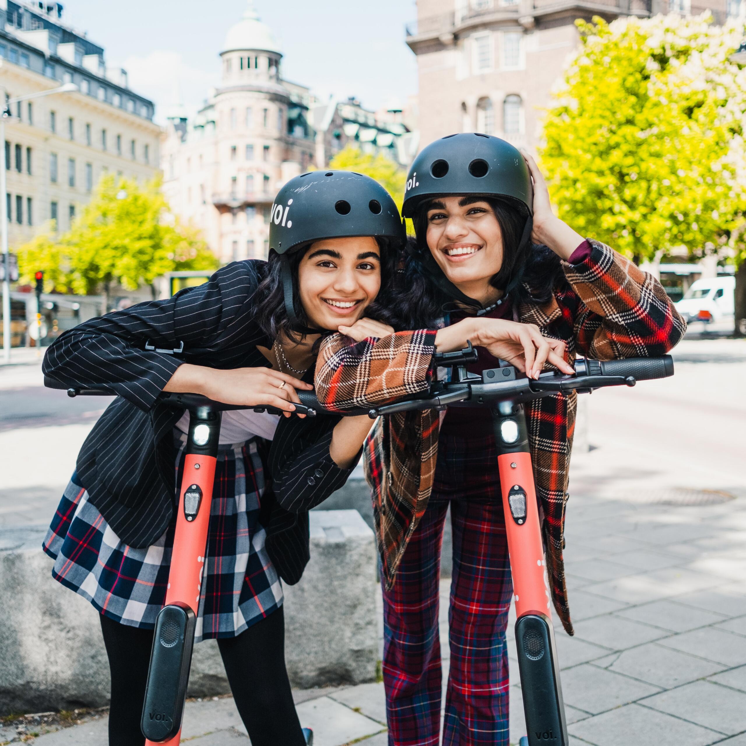 Photo of two young girls with Voi helmets and scooters posing in front of the camera