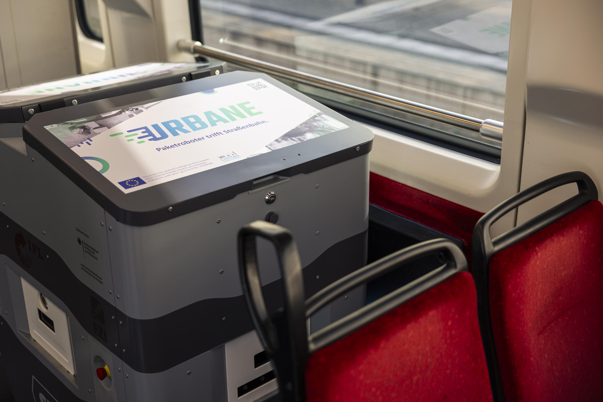 Photo of an autonomous delivery robot with the URBANE logo inside a tram