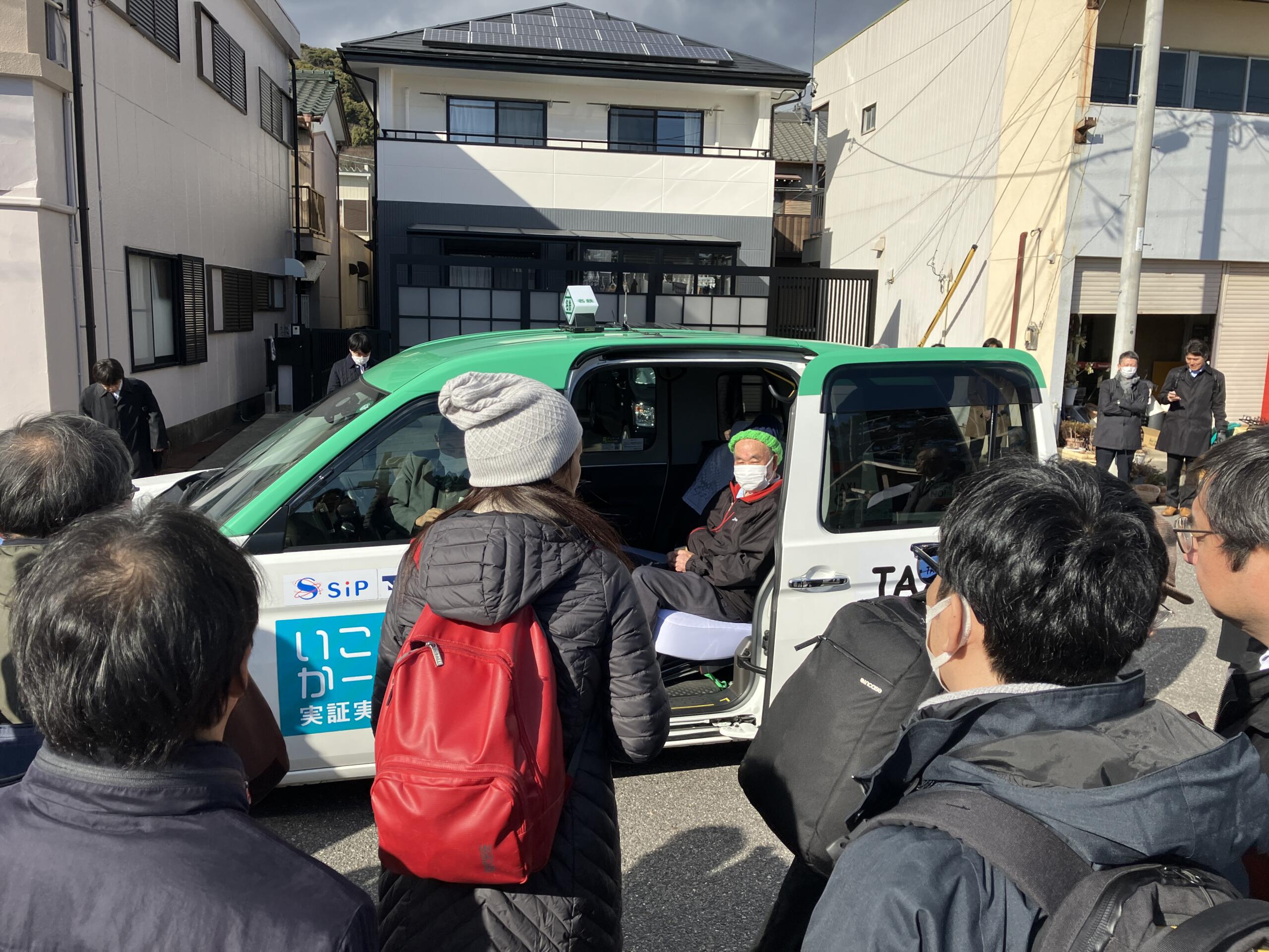 Photo of four people wearing winter jackets waiting for their turn to board a green taxi