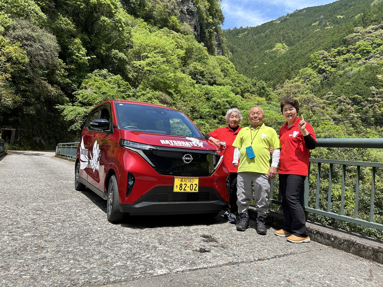 Photo of a young woman and a senior couple posing next to a red car