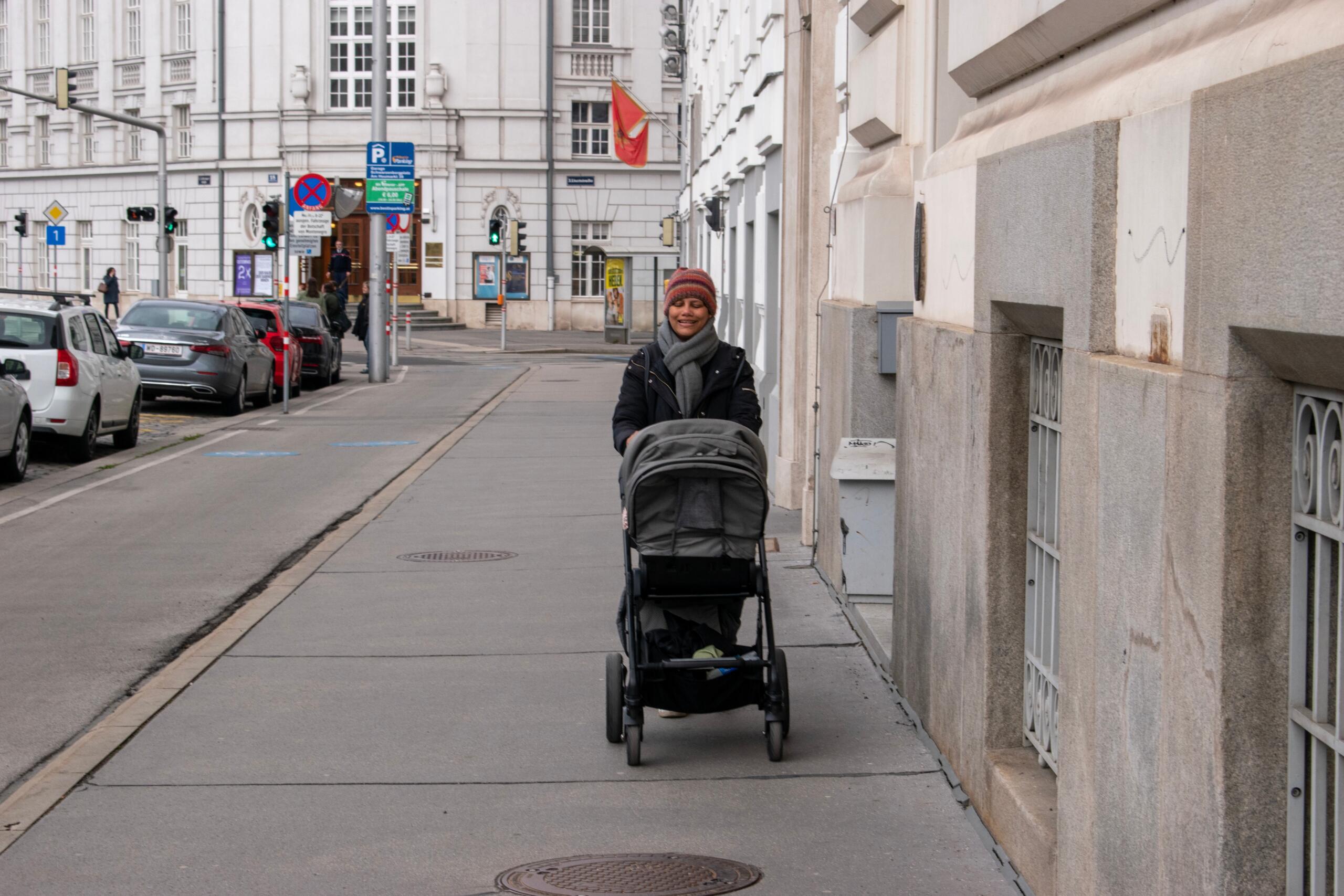 Photo of a woman with a stroller walking on a sidewalk in Vienna